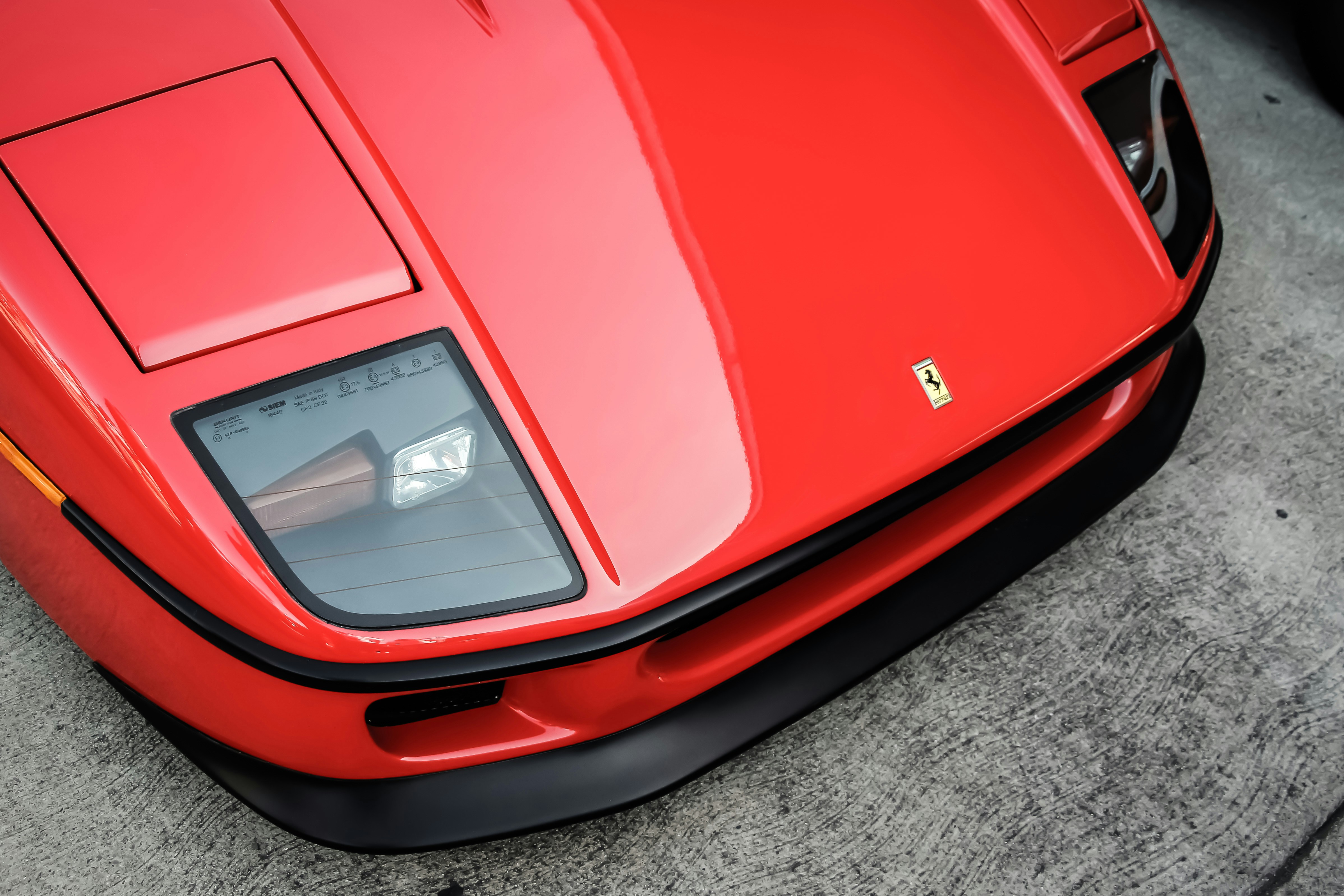 Close-up of the front section of a classic red Ferrari sports car, showing pop-up headlight housings, sculpted bodywork, a Ferrari badge on the bonnet, and glossy paintwork viewed from above.